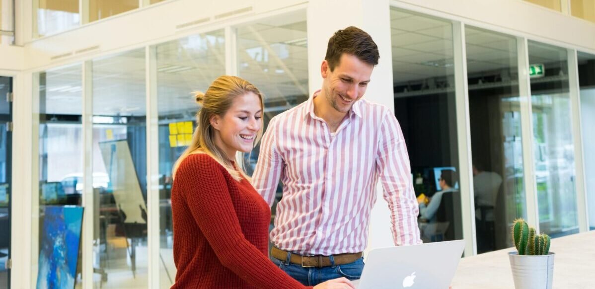 Two colleagues engaged in a positive discussion at a laptop in a modern office setting.