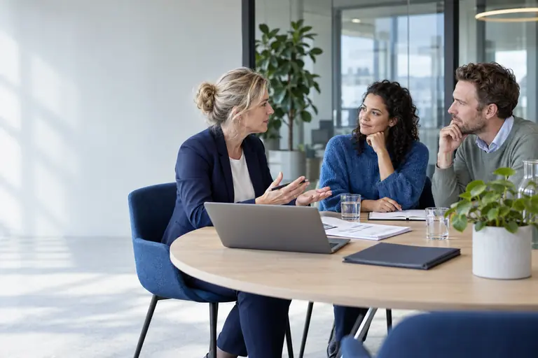 Arbeidsdeskundige in overleg met twee opdrachtgevers aan een vergadertafel