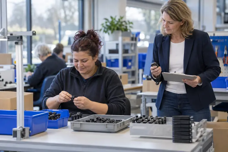 Arbeidsdeskundige observeert met een tablet de arbeidsprestatie van een medewerker aan de assemblagetafel