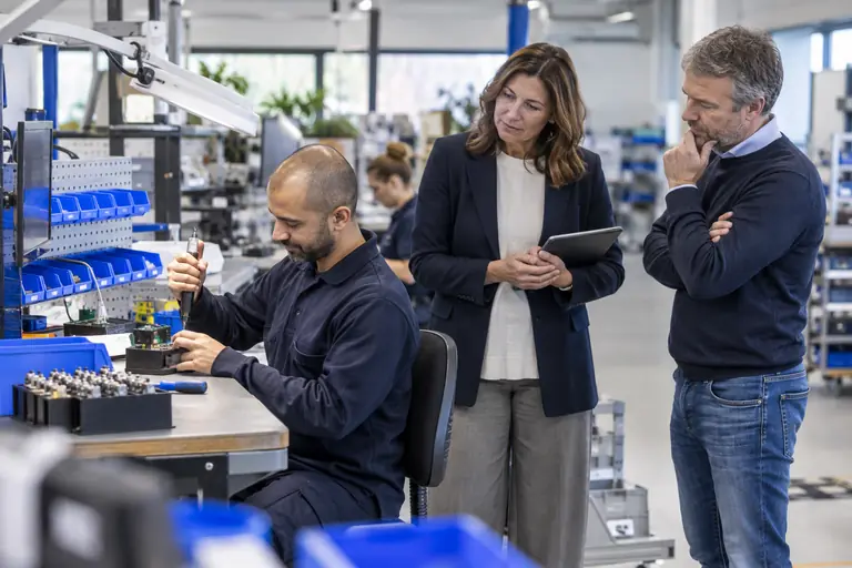 Arbeidsdeskundige met tablet beoordeelt de werkplek van een medewerker aan een assemblagetafel