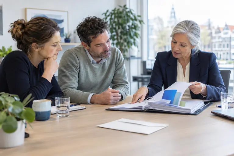 Drie mensen bespreken een dossier met tabbladen aan een tafel
