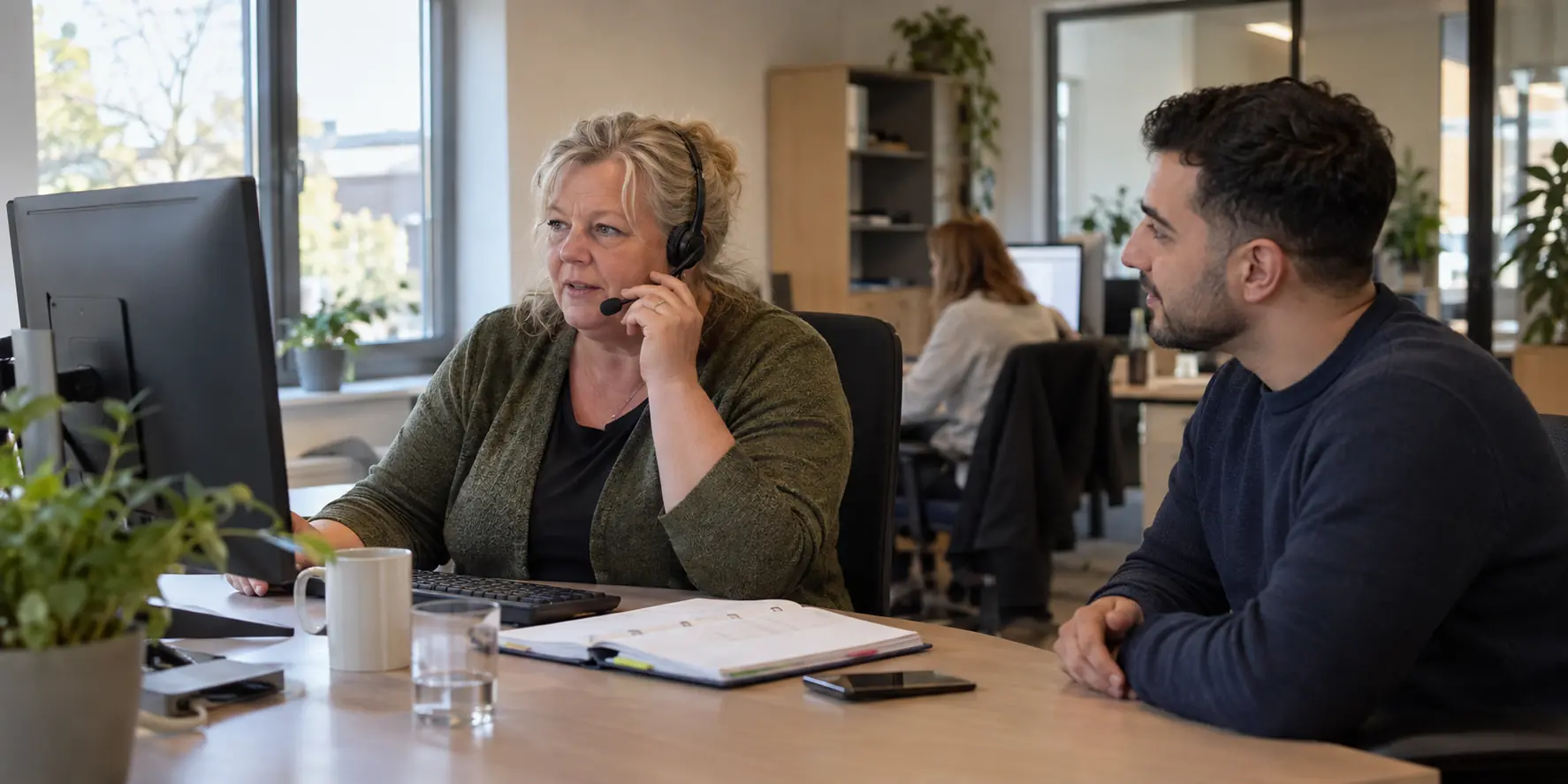 Twee professionals in gesprek aan een werkplek met beeldschermen
